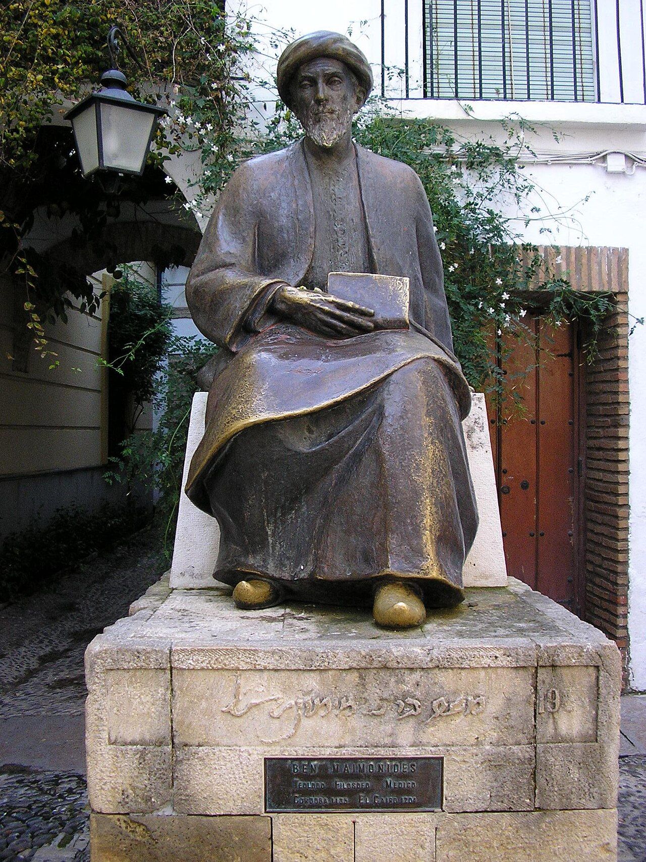 Bronze statue of a seated, bearded man in a turban and robe, holding a book